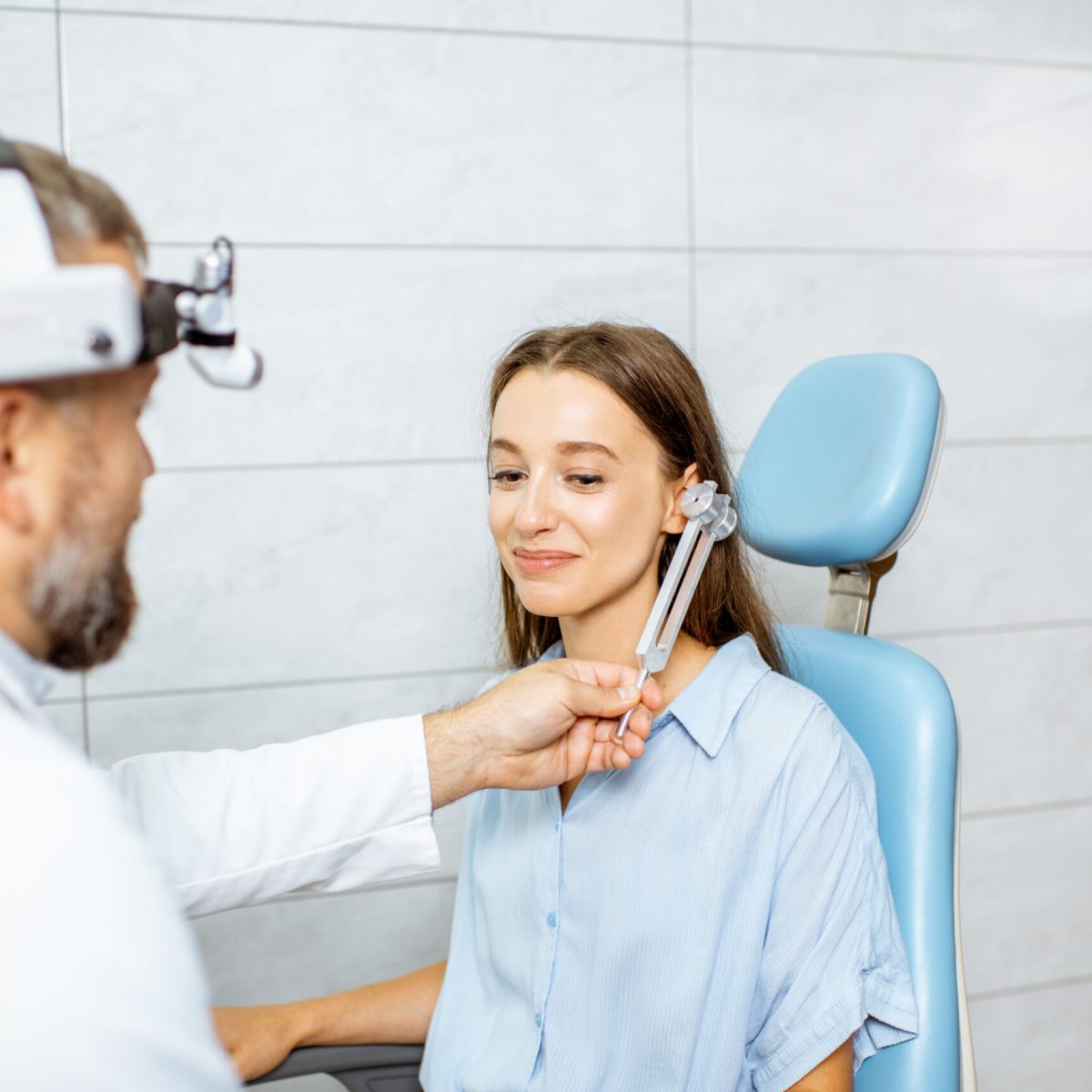 Hearing test with tuning fork Senior otolaryngologist examining ears with ENT tuning fork for a young patient in the medical office. Hearing test with tuning fork concept